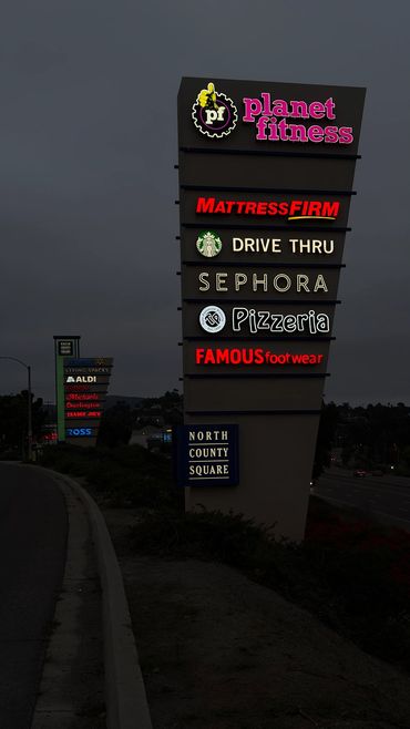 Illuminated shopping center signs at dusk alongside a highway.