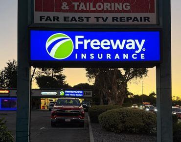 Illuminated Freeway Insurance sign at dusk in a small shopping plaza.