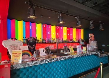 Colorful bar with rainbow decor and signage reading 'Ye Olde Gay Bar'.