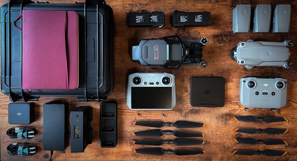 A wood table with 2 drones, two flight controllers, and various batteries and drone equipment on it.