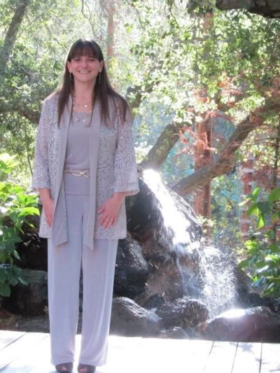 Woman in light gray outfit standing by a small waterfall.