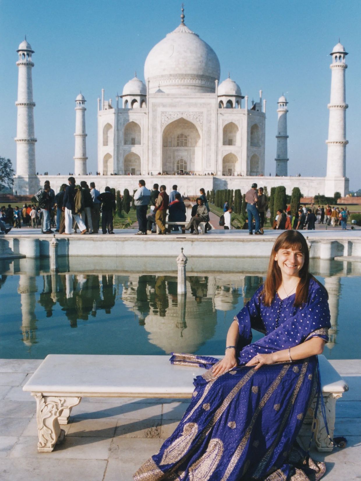 Woman in blue dress sitting by Taj Mahal reflecting pool.
