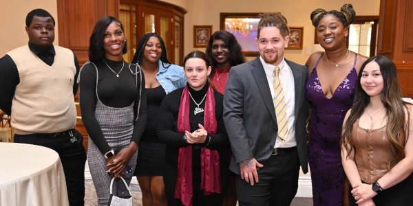 A diverse group of young adults dressed formally, posing indoors.