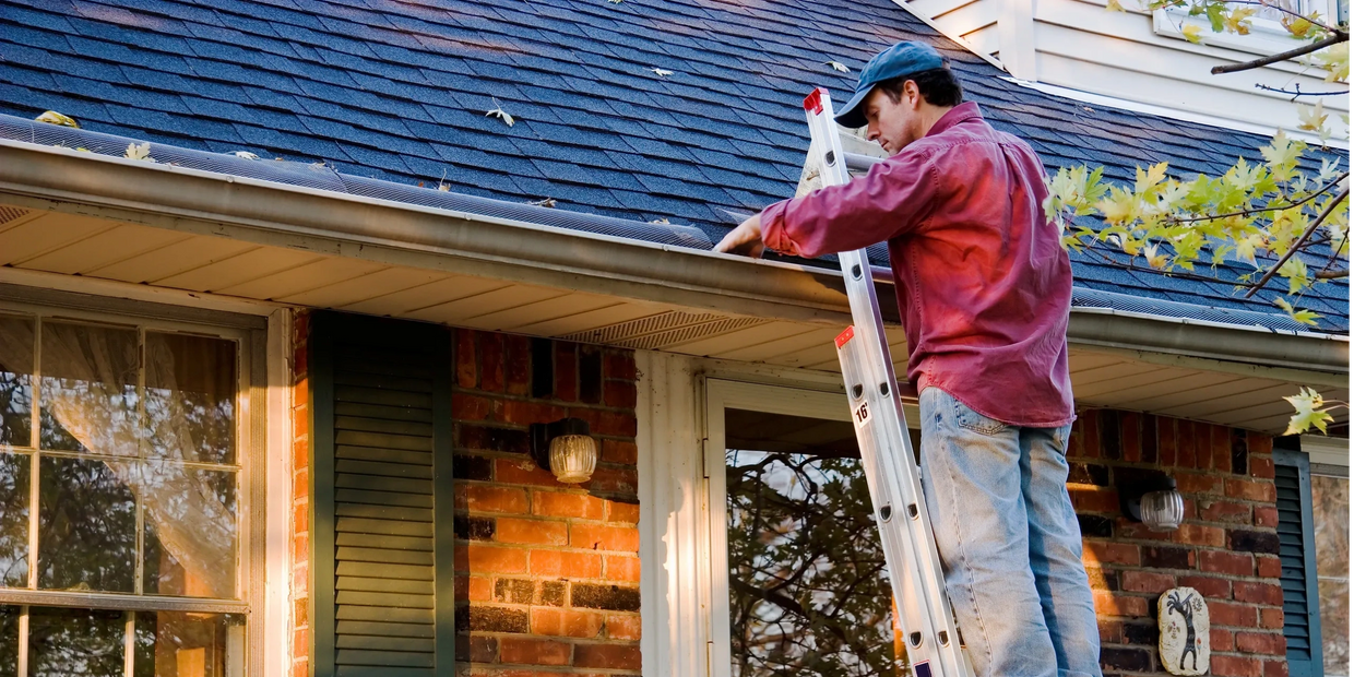 Handyman cleaning gutters in fall