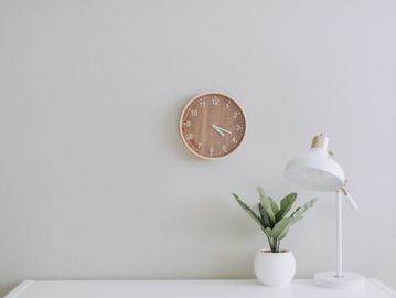 Minimalist desk setup with a clock, plant, and lamp.