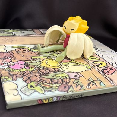 A small toy flower with green limbs sits on a colorful illustrated book cover.