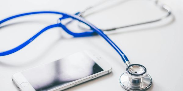 A stethoscope and smartphone on a white surface, symbolizing healthcare technology.