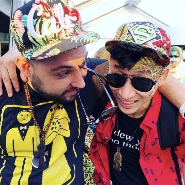 Two friends wearing colorful caps and smiling with their arms around each other.