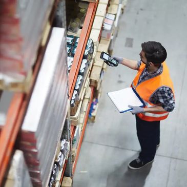 Warehouse worker scans inventory items on shelves using a handheld device.