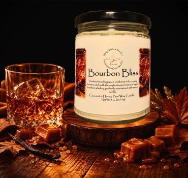Bourbon Bliss scented candle with whiskey glass and caramel on wooden table.