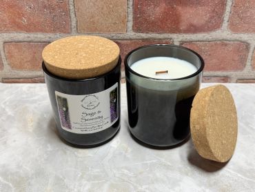Two black glass candles with cork lids on a marble surface and brick background.