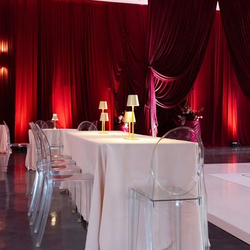 Elegant table setting with transparent chairs and red drapes.