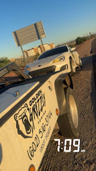 Tow truck towing a white sports car on a sunny day.