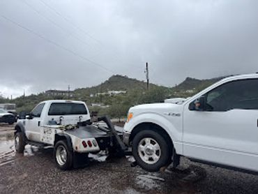 A tow truck pulling a white pickup truck on a cloudy day.