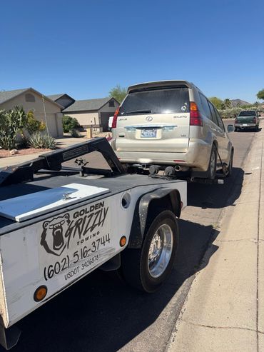 A Lexus GX470 being towed by Golden Grizzly Towing in a suburban neighborhood.
