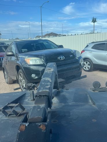 Black Toyota V6 SUV being towed on a dusty trailer in a parking area.