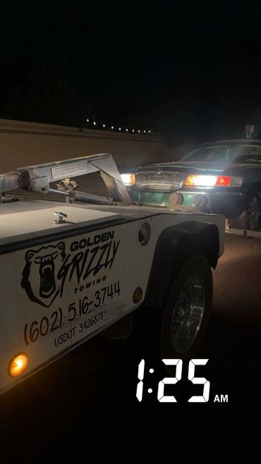 A tow truck from Golden Grizzly towing a car at night.