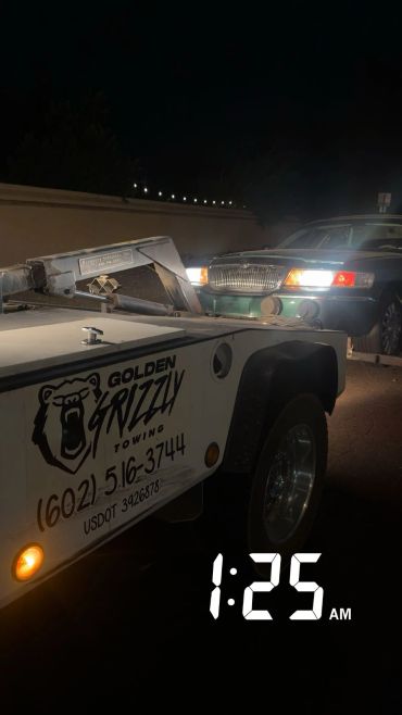 A tow truck from Golden Grizzly towing a car at night.