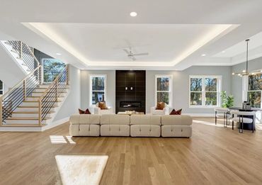 Bright modern living room with beige sofa, black fireplace, and wooden staircase.