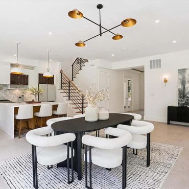 Modern dining area with black table and white chairs in an open kitchen space.