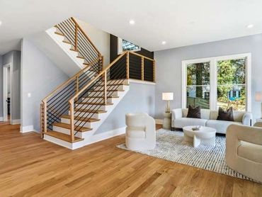 Bright modern living room with wooden staircase and neutral furniture.