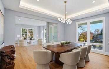 Modern dining room with wooden table and upholstered chairs under a stylish chandelier.