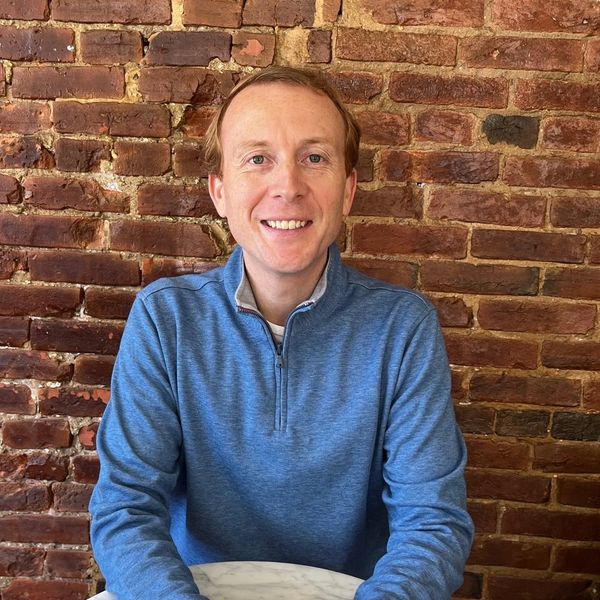Man smiling in blue sweater against brick wall.