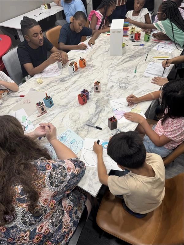 Children and an adult engaged in drawing and coloring at a large table.