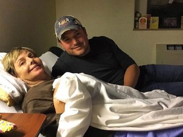 A woman lying in bed with a man beside her, both smiling gently.
