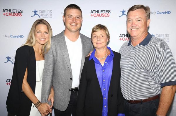 Four people posing together at an Athletes + Causes event with a branded backdrop.