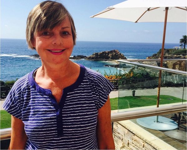 Smiling woman in a striped shirt by the ocean view on a sunny day.