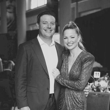 A smiling couple dressed elegantly at an indoor event.