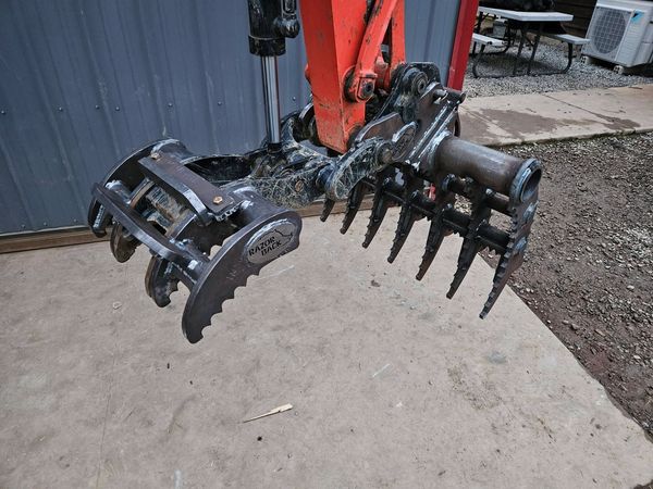 Excavator attachment with claw and rake tines for digging and grabbing.