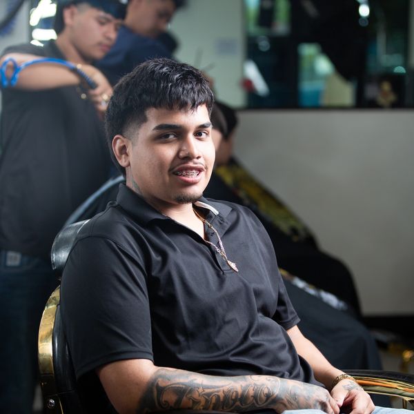 Young man with tattooed arm sitting in barber chair, smiling.