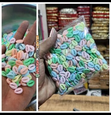 Colorful pastel beads shaped like cowrie shells held in hand and packed in a plastic bag.
