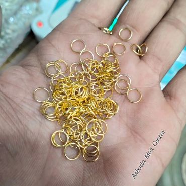 Hand holding small golden jump rings used in jewelry making.