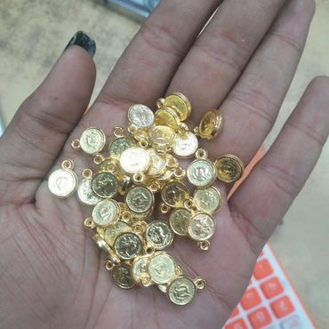 A hand holding several small, gold-colored coin charms with loops.