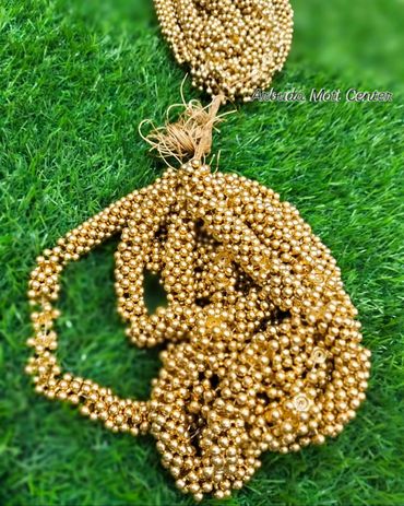 Golden bead necklace arranged on green grass.