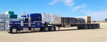 A blue Peterbilt semi-truck hauling tarped building materials