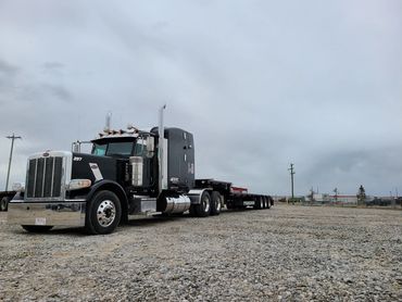 A clean black Peterbilt truck with a flatbed trailer parked