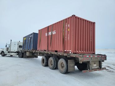 A Peterbilt semi-truck hauling containers on a flatbed trailer in snowy conditions