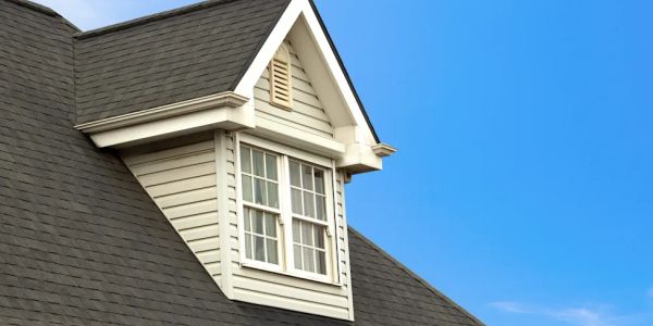 Dormer window on a house roof under clear blue sky.