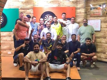 Group of men posing happily in a dart game room.