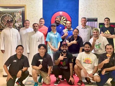 Group photo of people posing in front of a dartboard indoors.