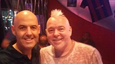 Two middle-aged men smiling together in a casual indoor setting.