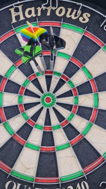 Three darts close to the bullseye on a Harrows dartboard.