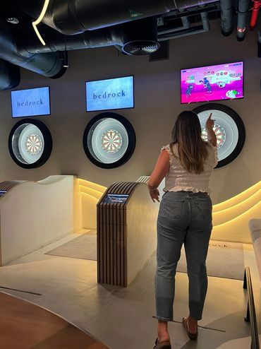 Woman playing darts in a modern indoor dart area with digital screens.