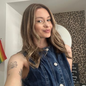 Young woman with tattoos and long hair smiling.