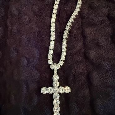 Diamond-studded cross pendant necklace on a dark textured surface.