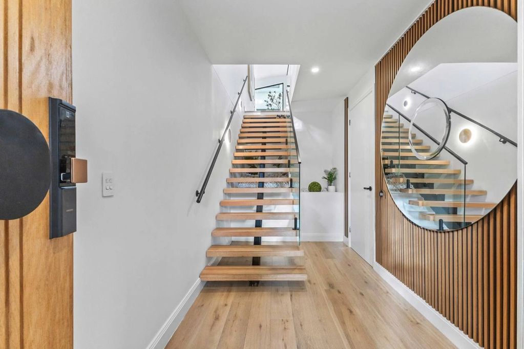 Modern staircase with wooden steps and glass railing in a bright hallway.